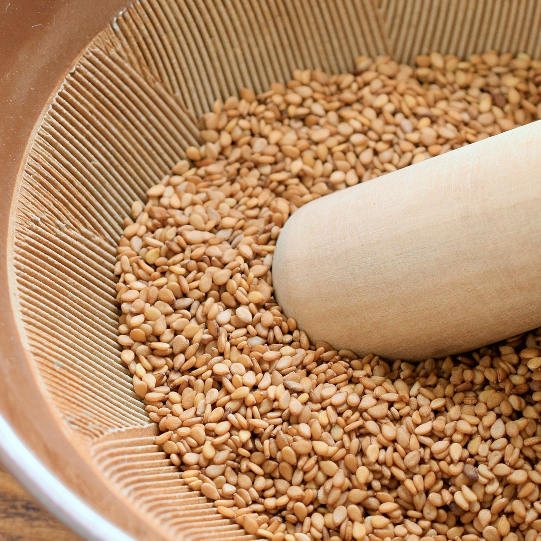 Roasted sesame seeds being ground into paste in a Japanese suribachi mortar