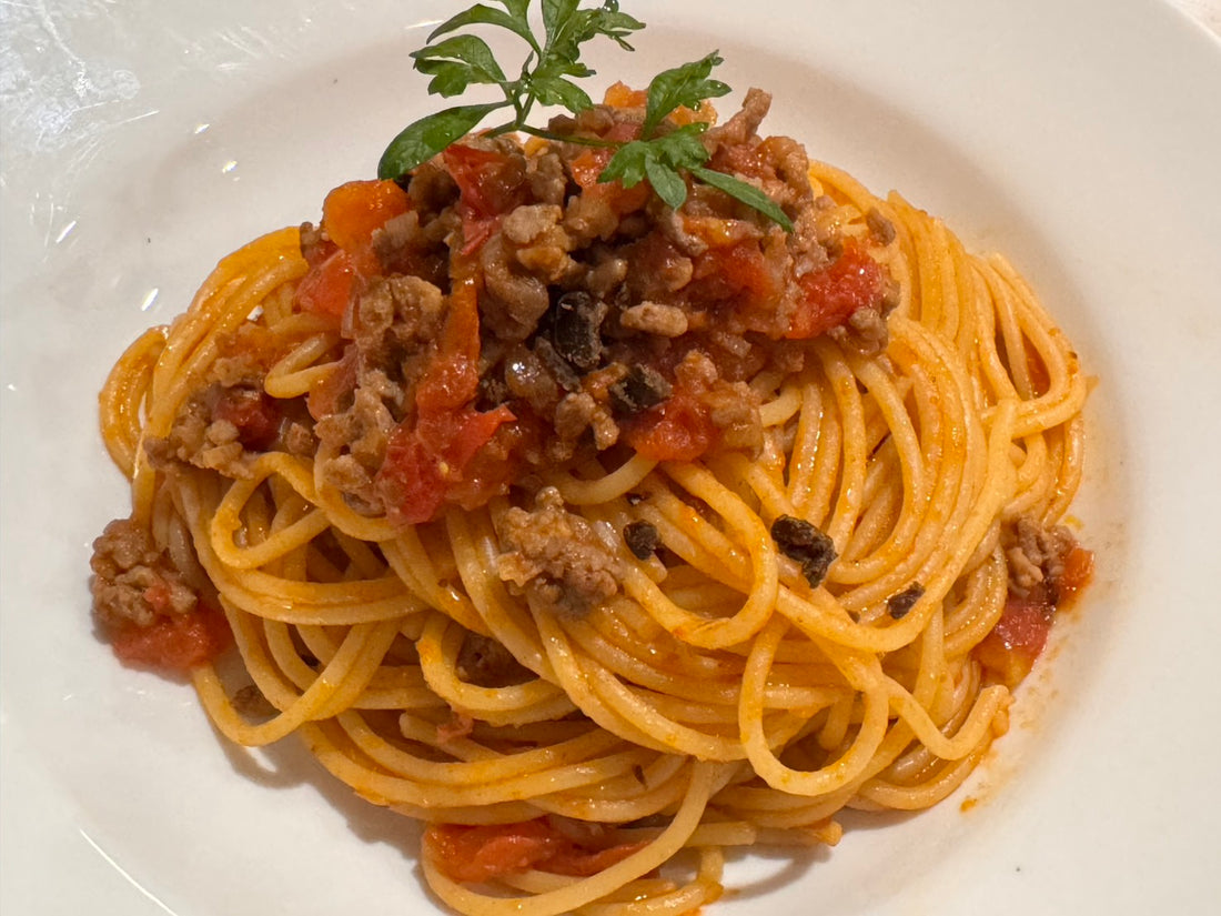 A plate of spaghetti bolognese made with hamanatto, centered on a white plate with parsley garnish