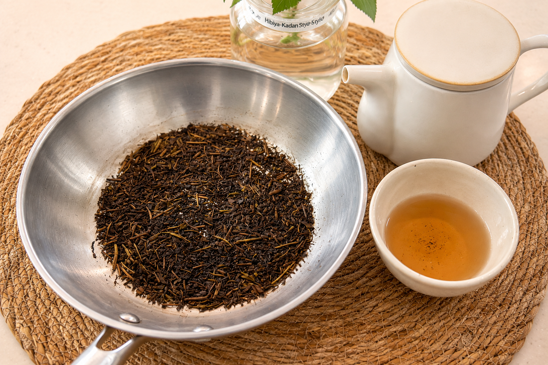 Roasted hojicha in a pan beside a teapot and a cup of freshly brewed tea
