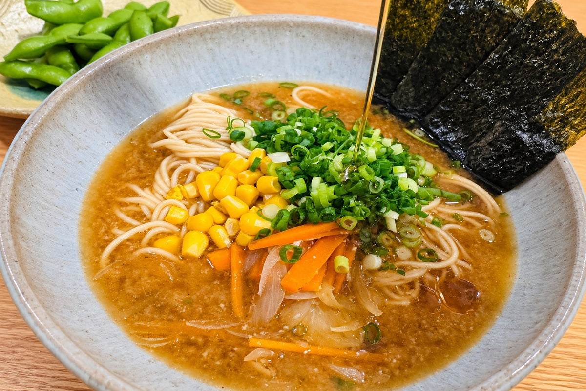 A thread of sesame oil poured over a bowl of vegan miso ramen with sweet corn, scallion, carrot and nori