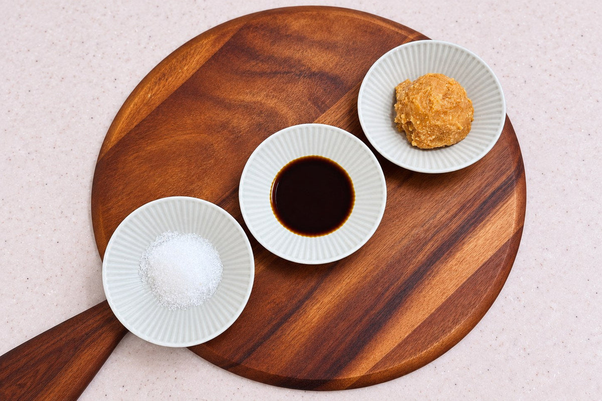 Three small dishes on a round wooden board — salt, soy sauce and miso, the three seasonings a bowl of ramen is named after
