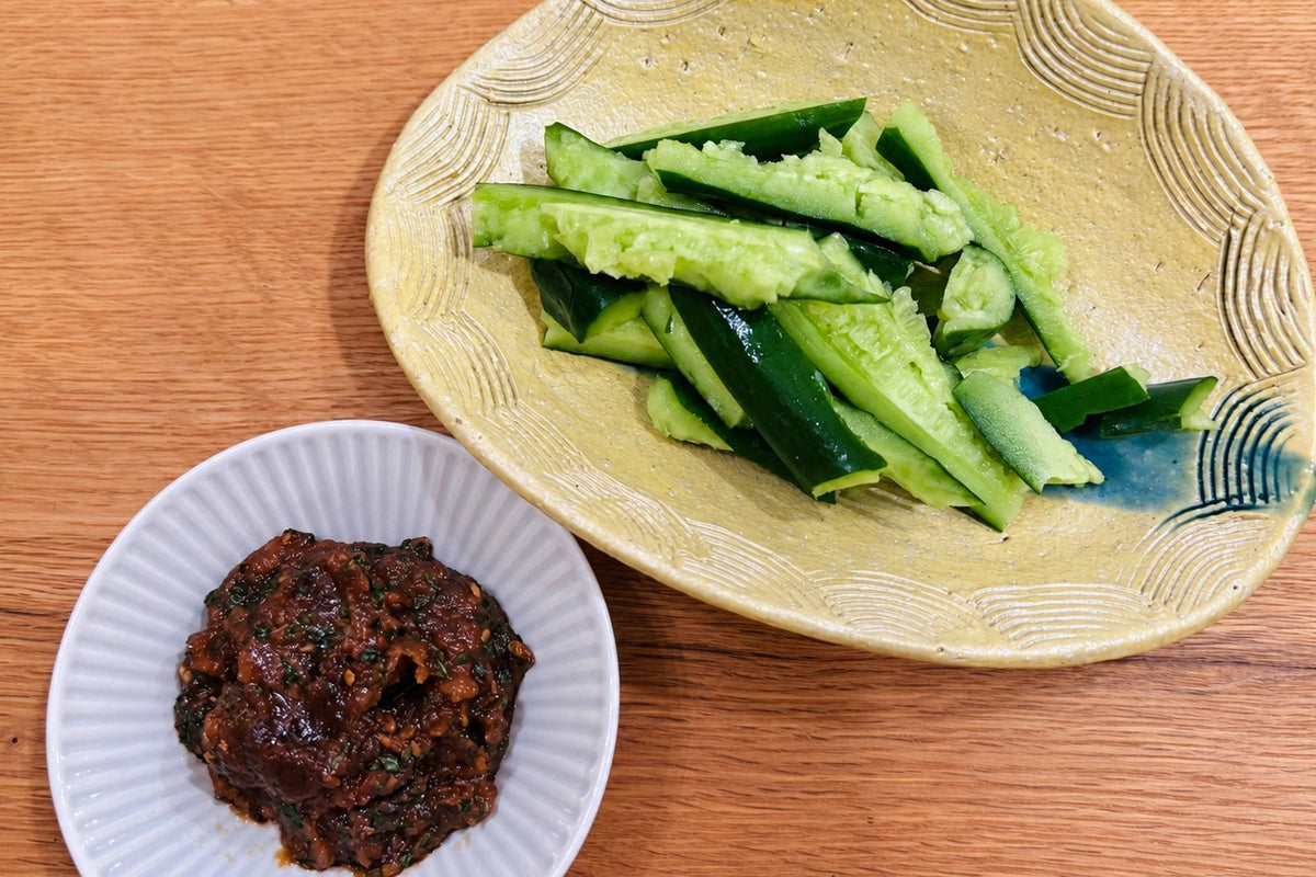 A dish of smashed cucumber beside a small plate of dark green shiso miso