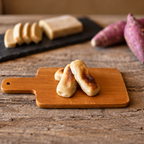Toasted kankoro mochi on a small wooden board, with the bar, sliced pieces and sweet potatoes behind