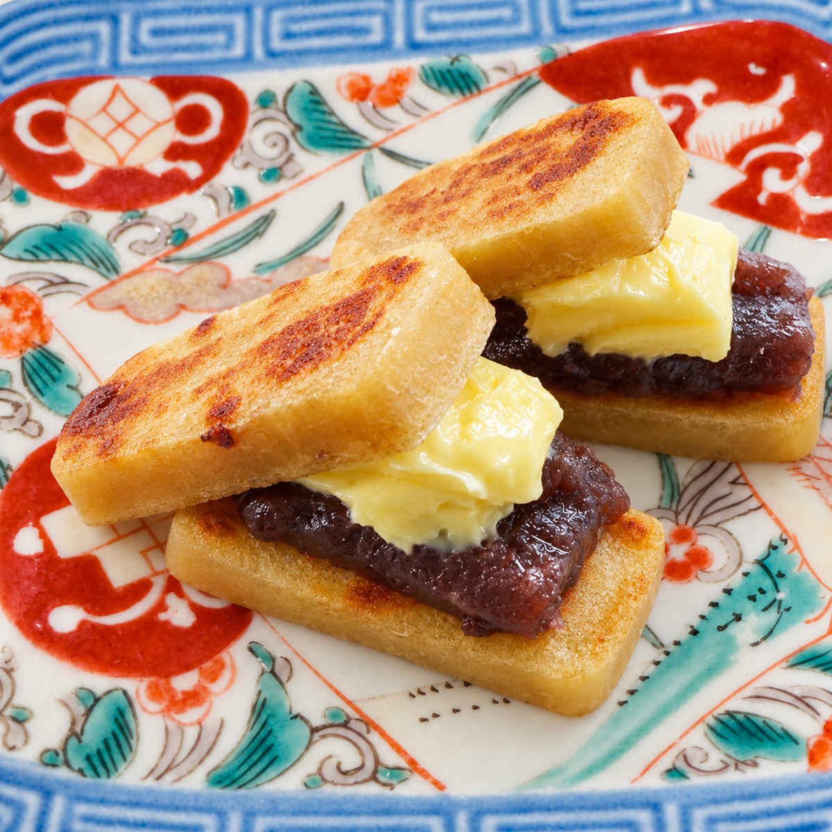 Toasted kankoro mochi sandwiches filled with sweet red bean paste and butter, on a patterned plate