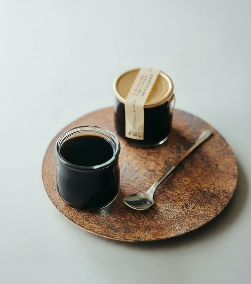 Two jars of dark liquid on a wooden tray with a spoon, on a white background